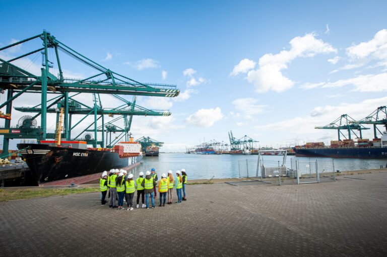 Studenten hoger onderwijs staan aan de kade in de haven en krijgen uitleg van een gids tijdens een havenbezoek. © Kris Jacobs